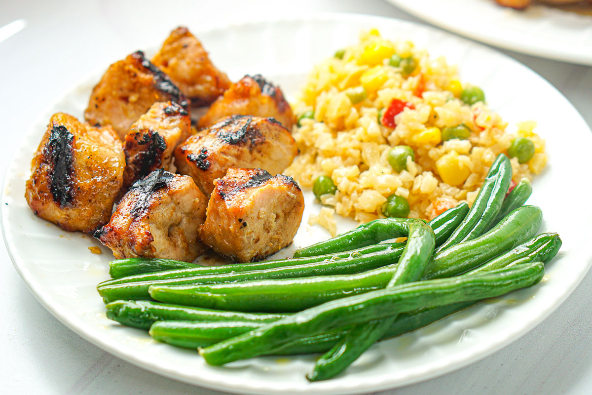 white plate with pork cubes, cauliflower rice and green beans