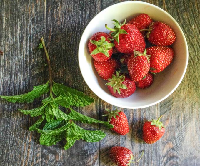 white bowl of fresh strawberries and a sprig of mint