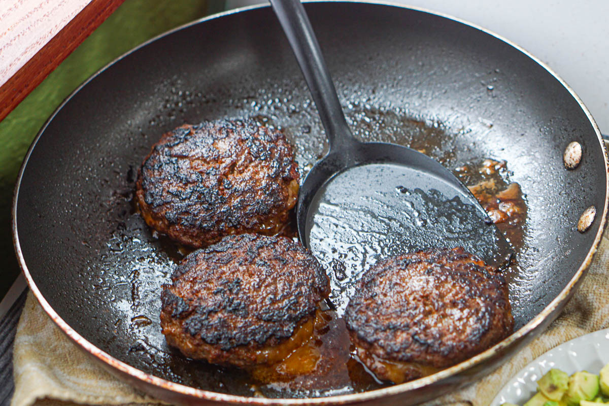 skillet with 3 burgers and a spatula