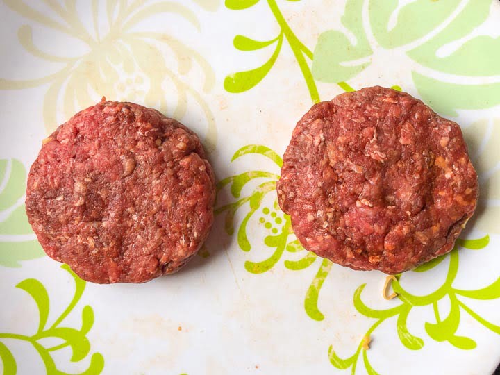 green and white plate with two cheddar stuffed burgers ready to be cooked 