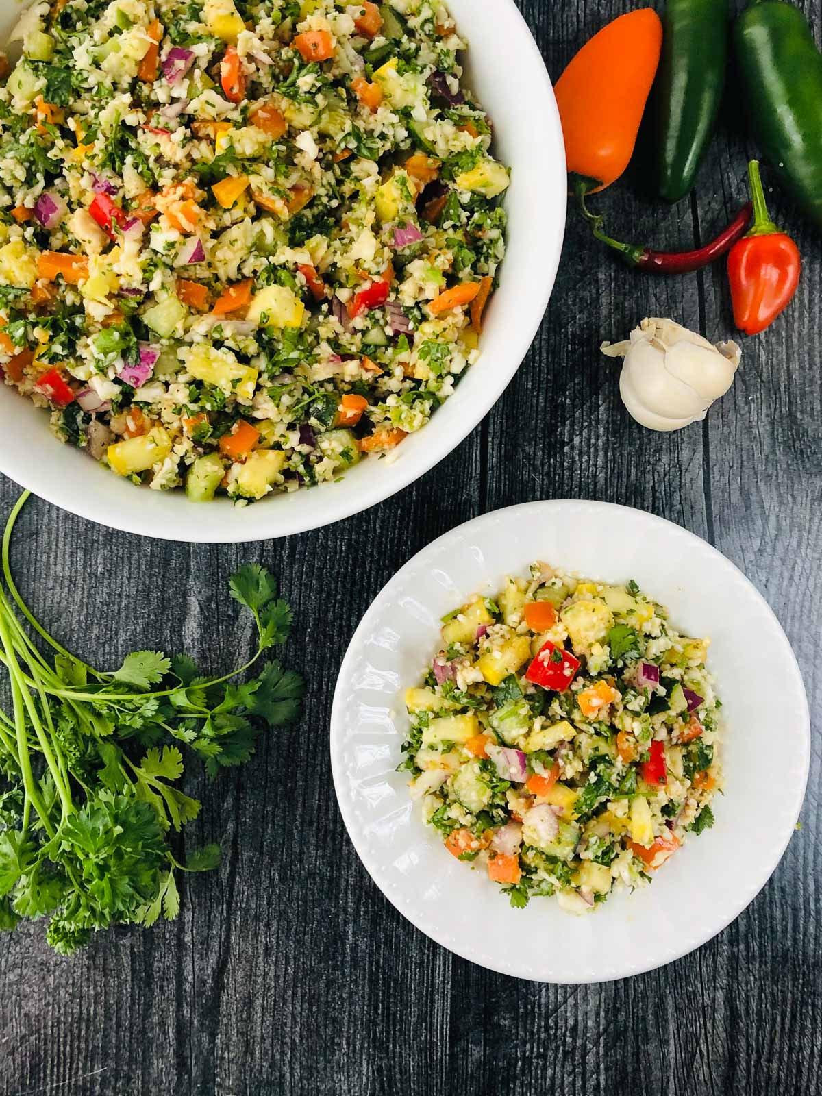 aerial view of a bowl and plate with keto tabouli salad and fresh herbs and veggies 