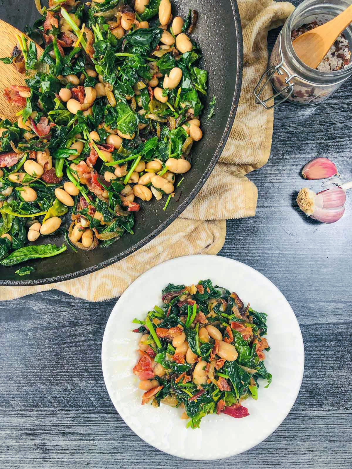 aerial view of a pan and plate with white beans and greens with bacon