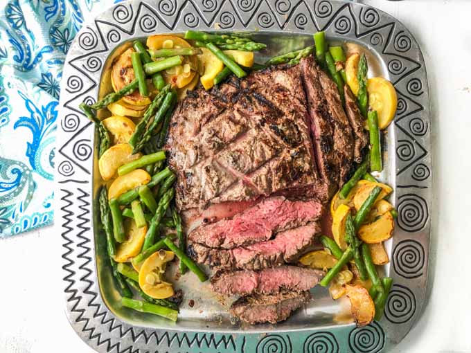 silver platter with grilled marinated flank steak and vegetables