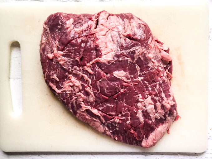 raw flank steak that is scored in a diamond pattern on a white cutting board