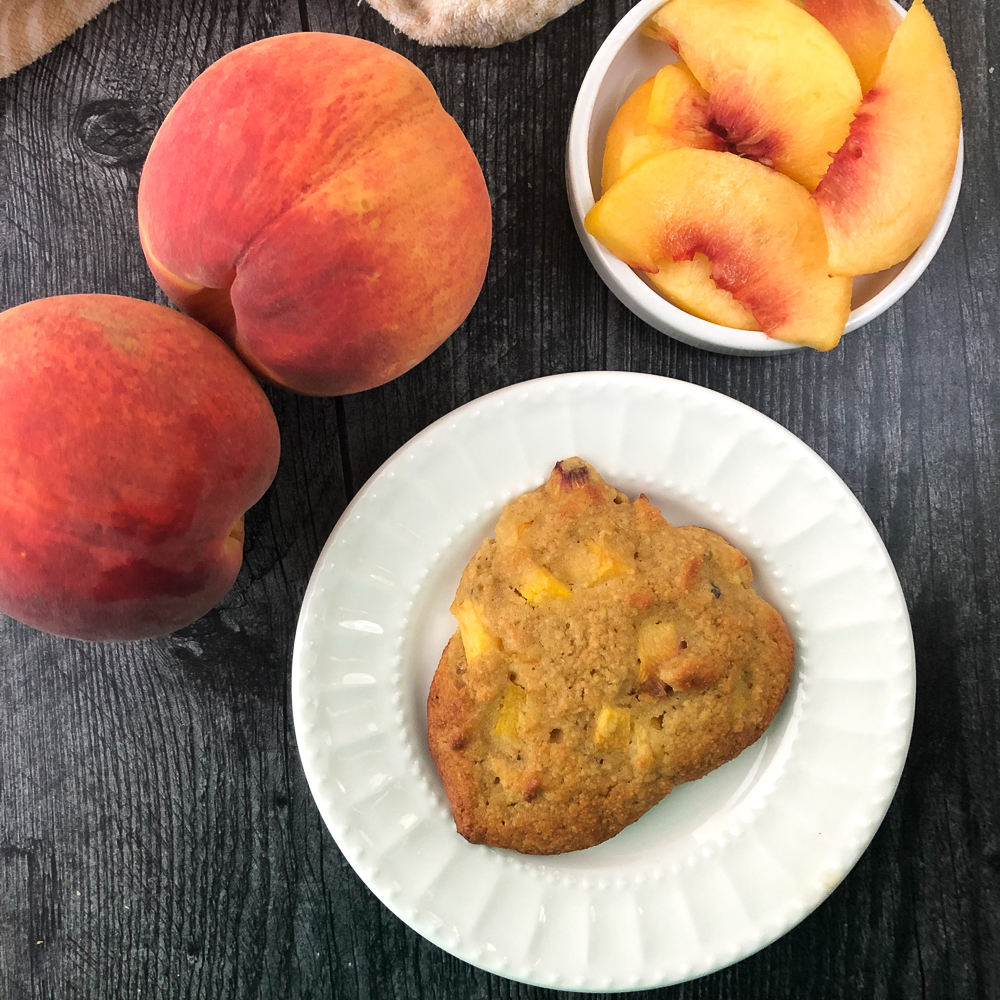 white plate with low carb peach scone and fresh peaches around it