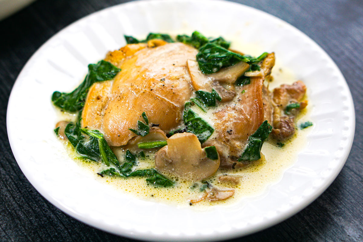 Closeup of a white dish with a serving of the creamy chicken thighs.