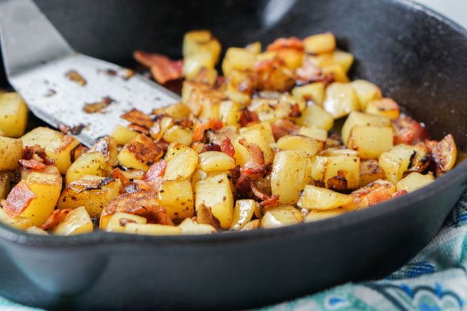 cast iron skillet with fried diced potatoes and bacon and a spatula