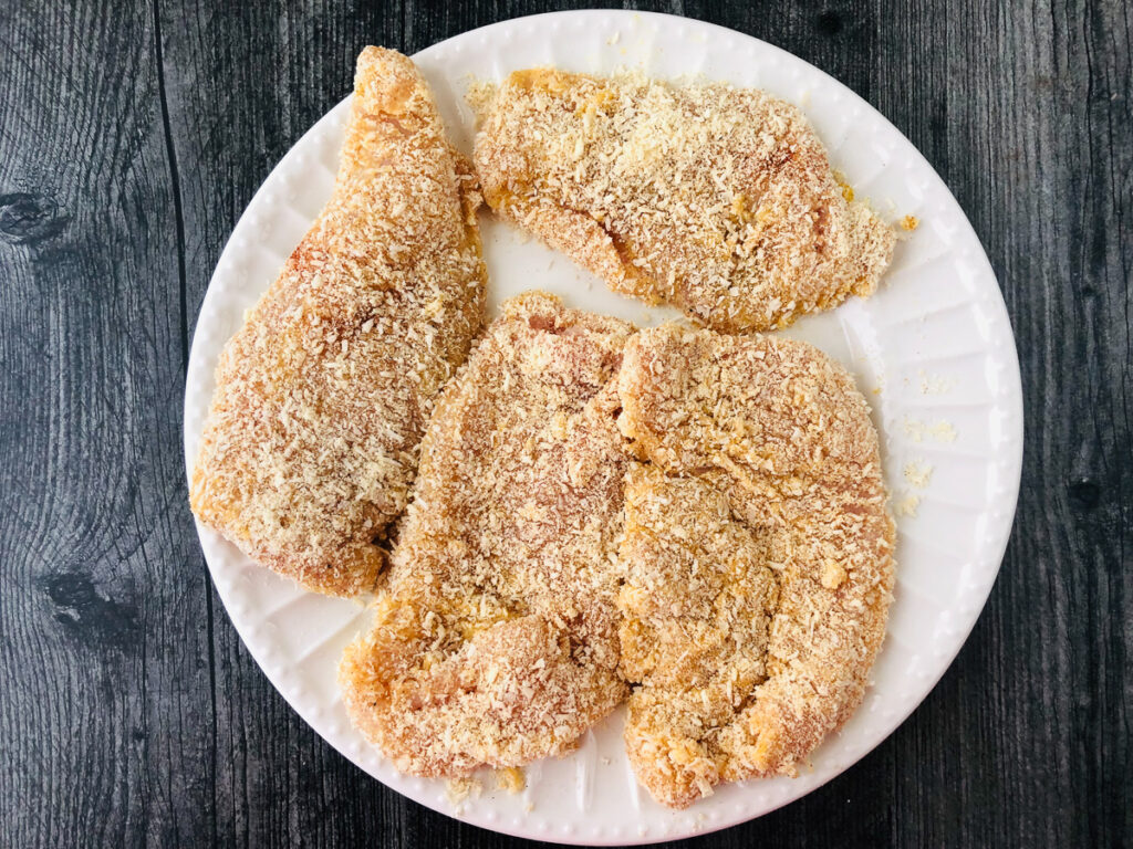 white plate with breaded raw chicken breast