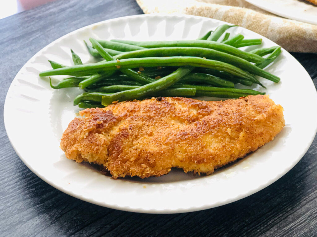 closeup of white plate with green beans and coconut crusted chicken