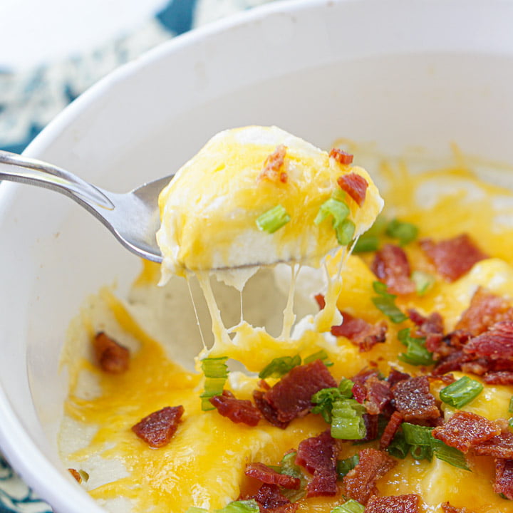 closeup of a spoonful of loaded cauliflower mash with bacon crumbles and stringy melted cheese