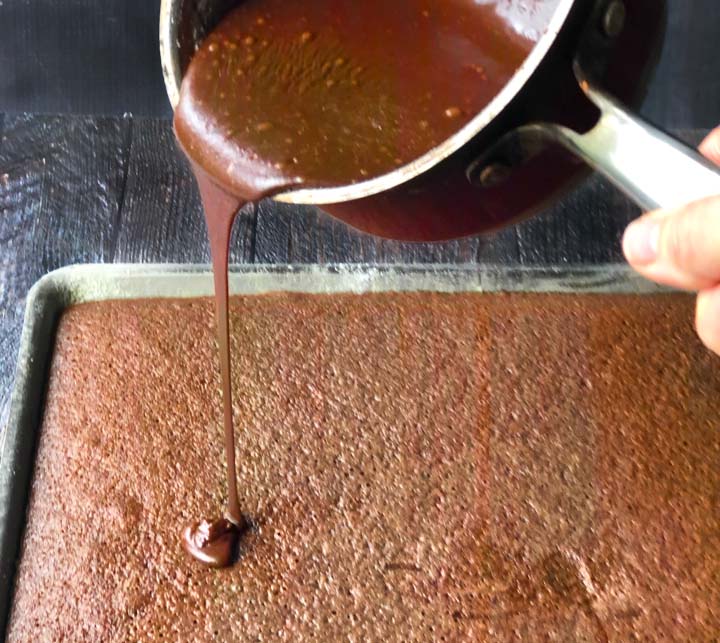 chocolate icing being poured from a pan onto the sheet cake  that just came out of the oven.