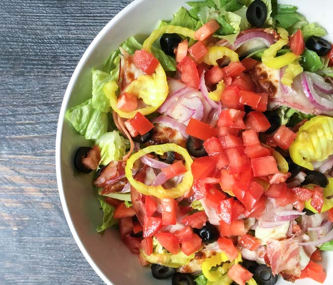 big colorful bowl of Italian sub salad with pepper rings, olives, tomatoes baked meats and cheeses and romaine