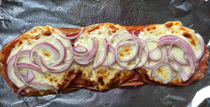 piece of foil with baked lunch meat slices, cheese and red onions coming out of the oven