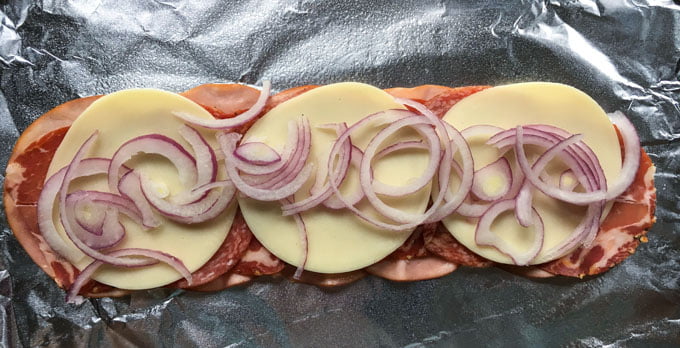 piece of foil with lunch meat slices, cheese and red onions