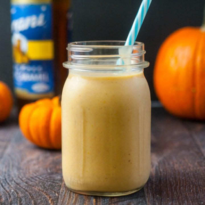 mason jar of low carb salted caramel pumpkin smoothie with blue straw, pumpkins and Torani bottle