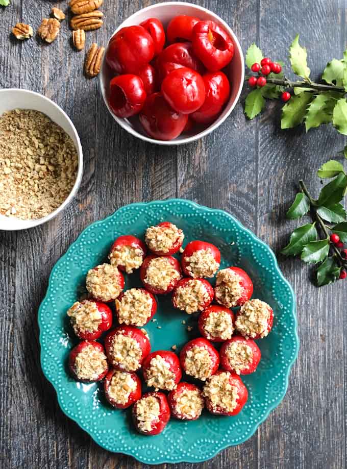 green plate with goat cheese stuffed pepper appetizer, crushed nuts, bowl of peppadews  and a sprig of holly