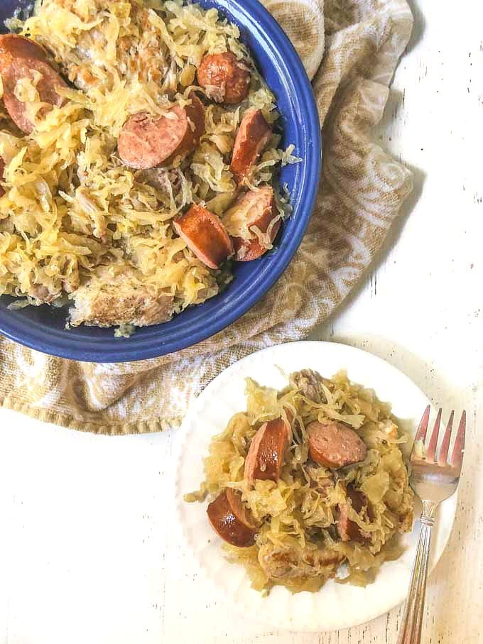 blue bowl with pork and sauerkraut and kielbasa and a white plate with a serving