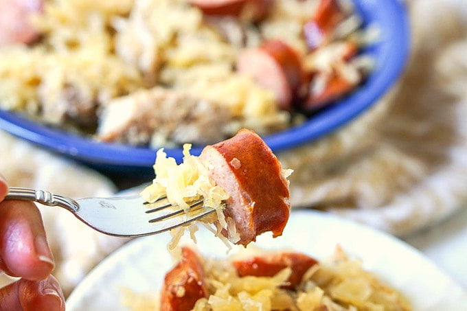 forkful of kielbasa and sauerkraut with blue bowl in background