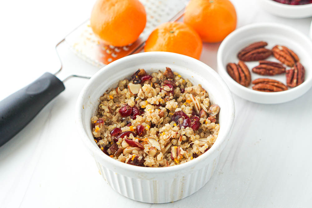 ramekin of hot quinoa with cranberries and fresh oranges & pecans in the background