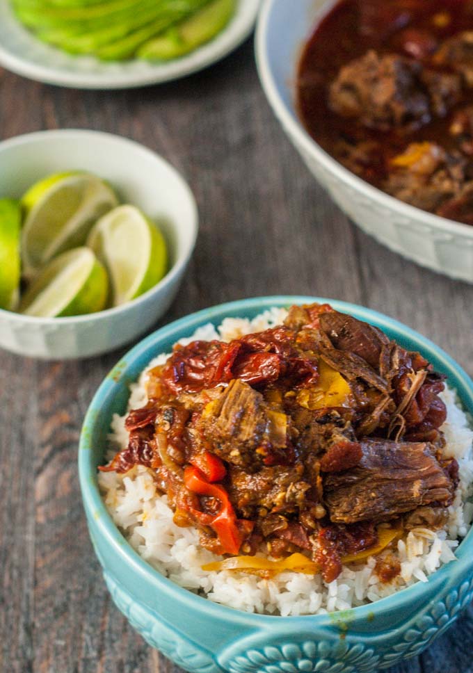 Blue bowl of rice and Barbacoa beef with a bowl of limes in the background.