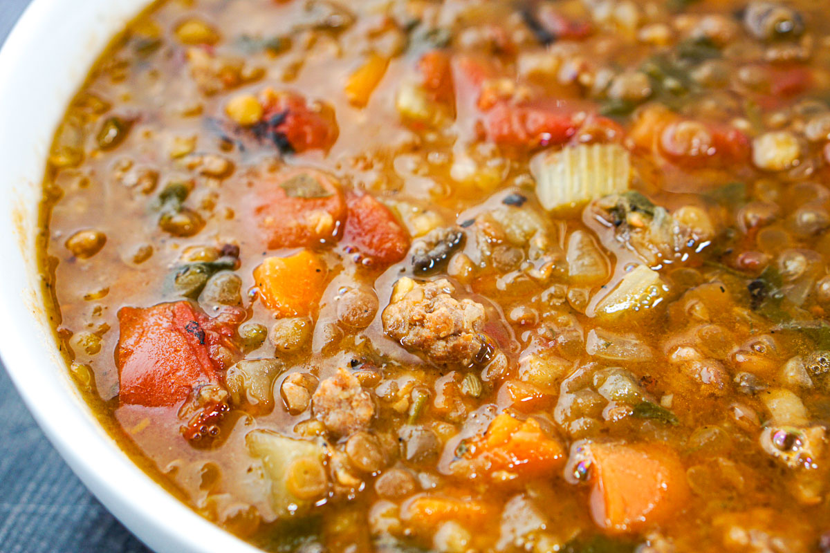 closeup of a white bowl of hearty lentil and sausage soup