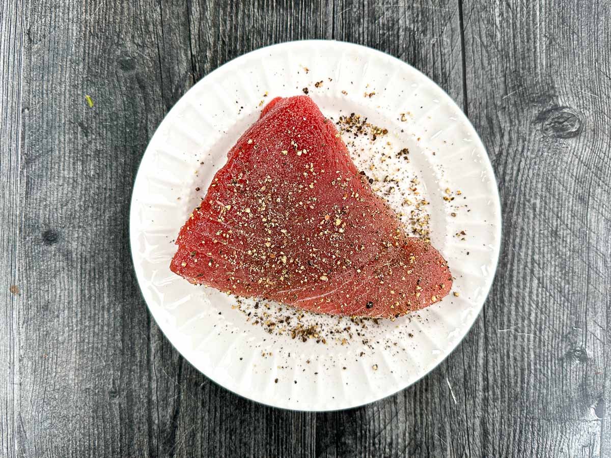 white plate with raw fresh tuna covered in salt and pepper. 