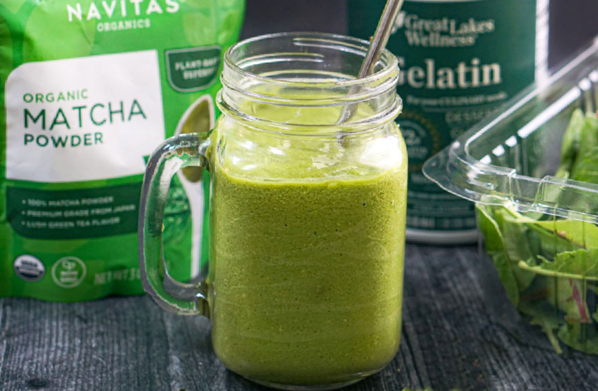 Closeup of finished matcha drink with the bag of green tea behind it and a bottle of gelatin and mixed greens.