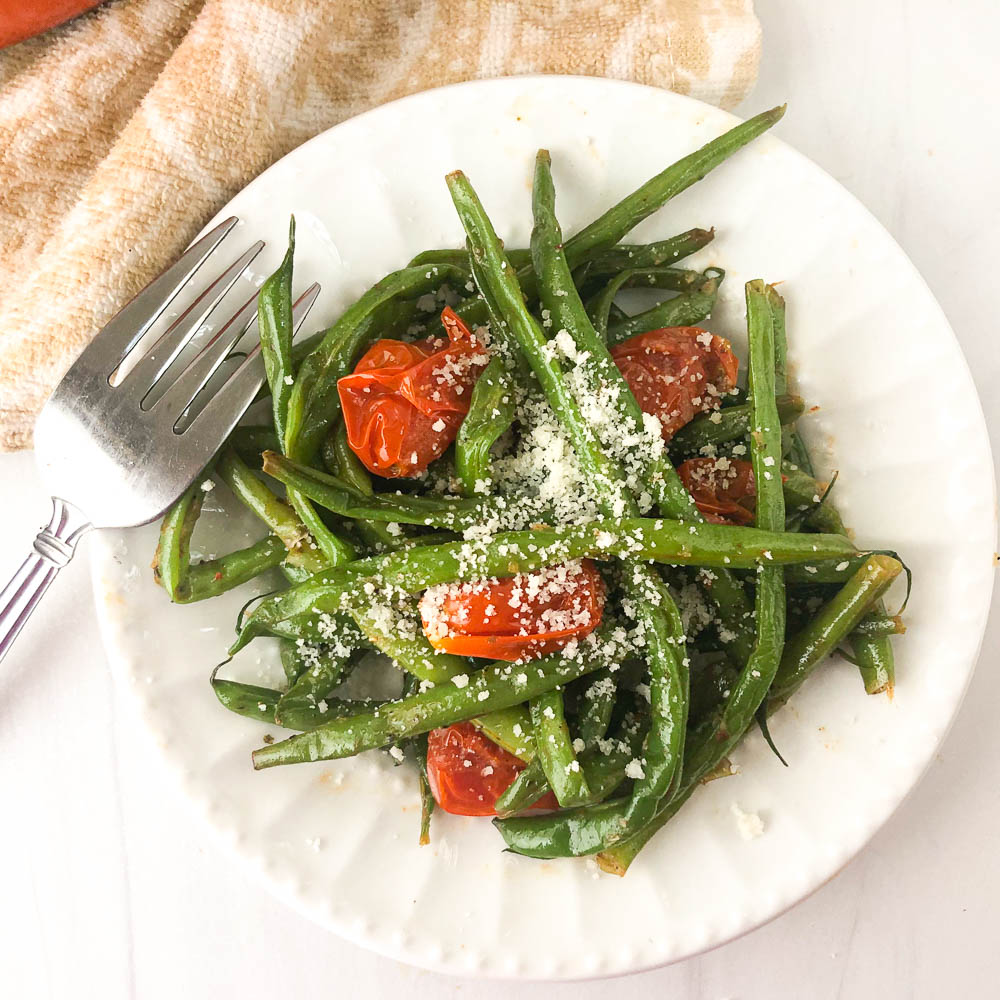 white plate with green beans and tomatoes side dish and a fork