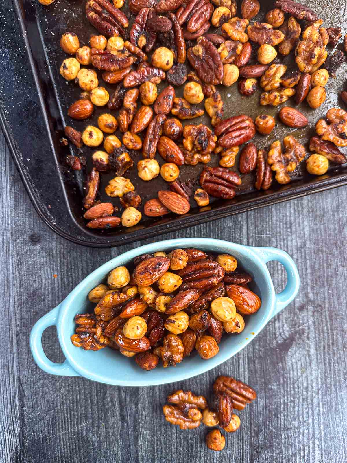 Slow Cooker Thai Curry Nuts - a great low carb snack in minutes with a few ingredients. Aerial view of a sheet pan and blue bowl with spicy mixed nuts.
