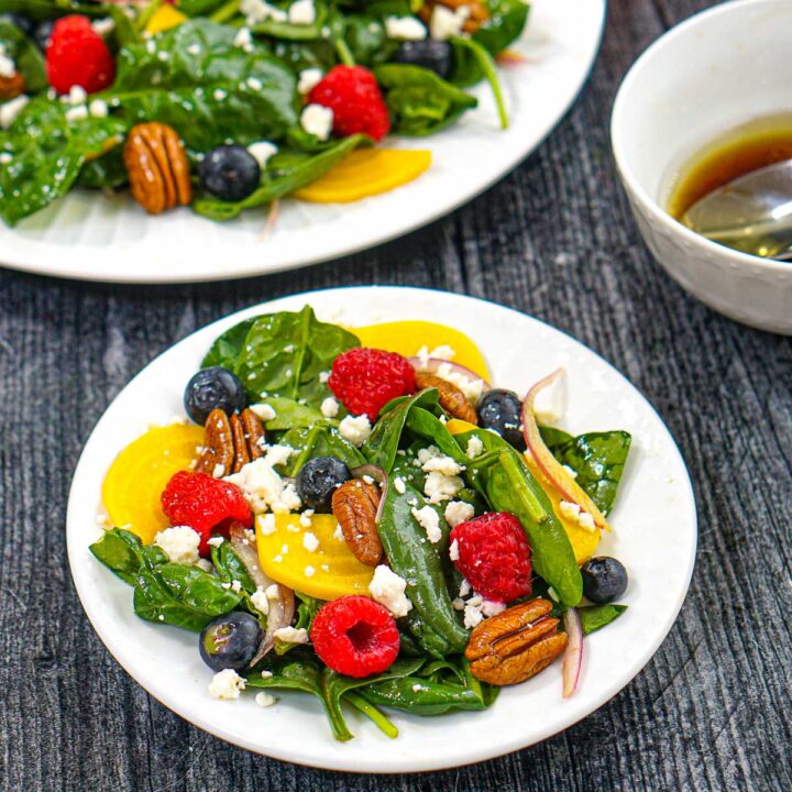 Closeup of a white plate with pickled beet salad with berries, pecans and gorgonzola cheese.