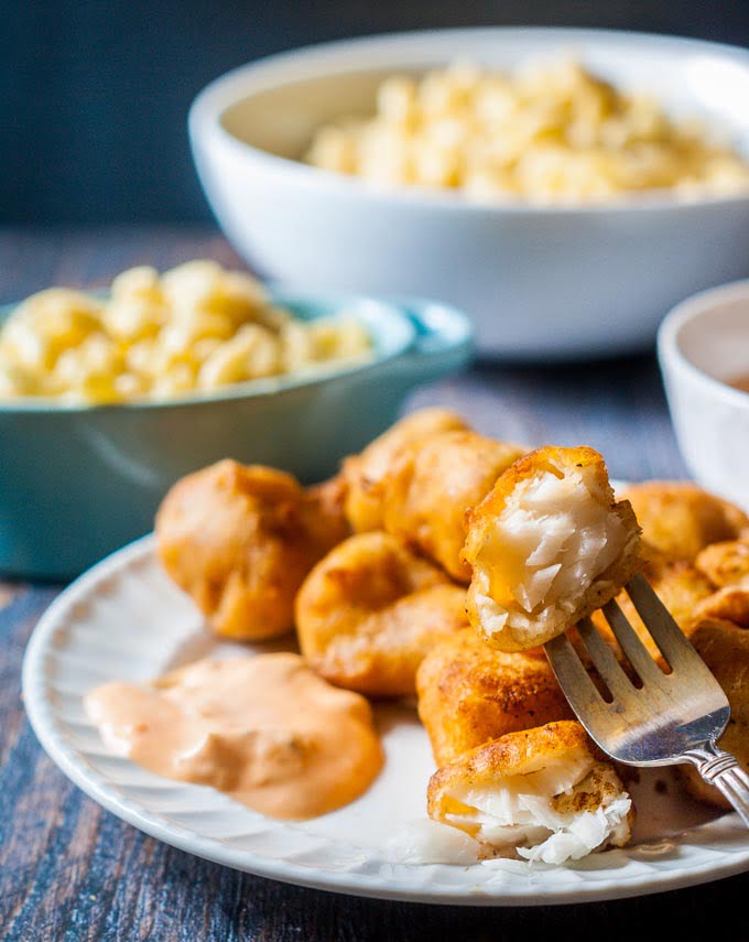 plate of battered fish nuggets with a fork with Mac and cheese in the background.