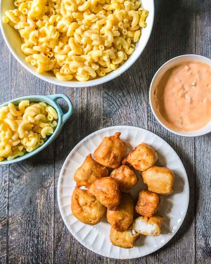 Plate of battered fish nuggets with a bowl of Mac and cheese and sriracha tarter sauce.