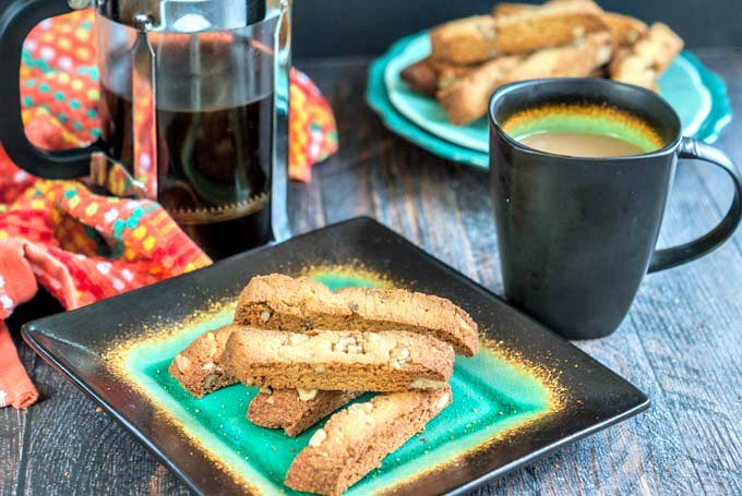 green and black plate with gluten free biscotti and coffee press in background with a cup of coffee