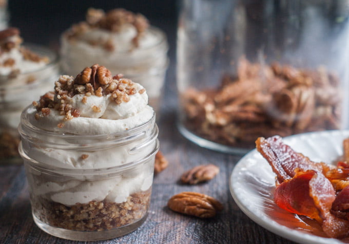 small jars with maple bacon low carb cheesecake, a plate of bacon and a jar of raw pecans