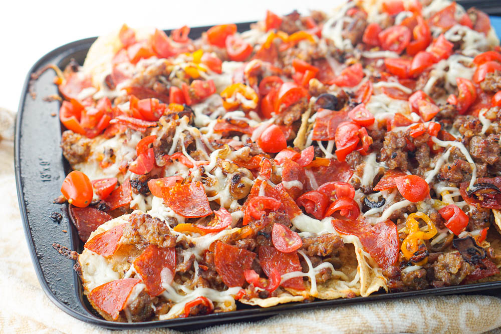 closeup of tortilla chips topped with sausage, peppers, pepperoni, cheese and tomatoes