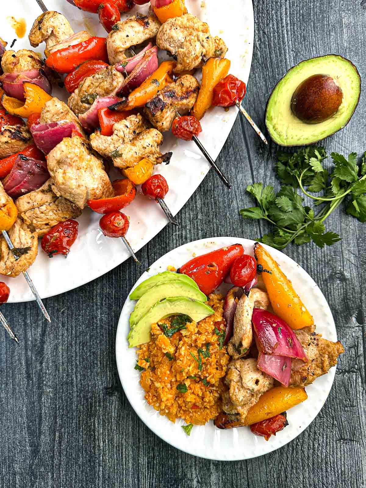 Grilled Chicken Fajita Kebabs - easy, healthy tasty dinner - make tacos or eat over a salad! Aerial view of a platter of keto chicken fajita skewers and plate with a serving and Mexican cauliflower rice.