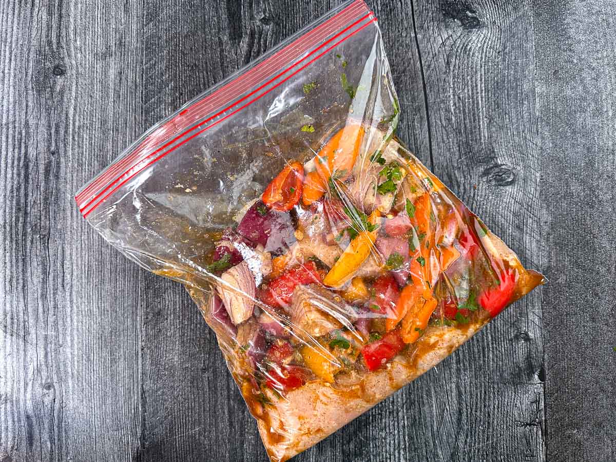 Ziplock bag with the raw chicken and veggies in the fajita marinade.