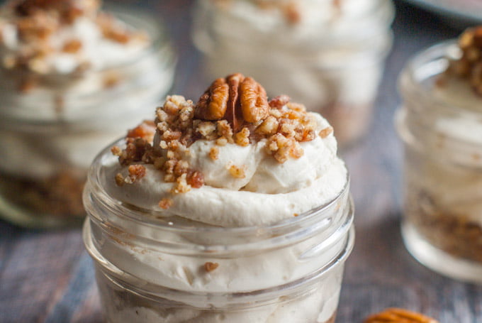 closeup of a top of small jar of no bake cheesecake with nut crumbles and a pecan on top