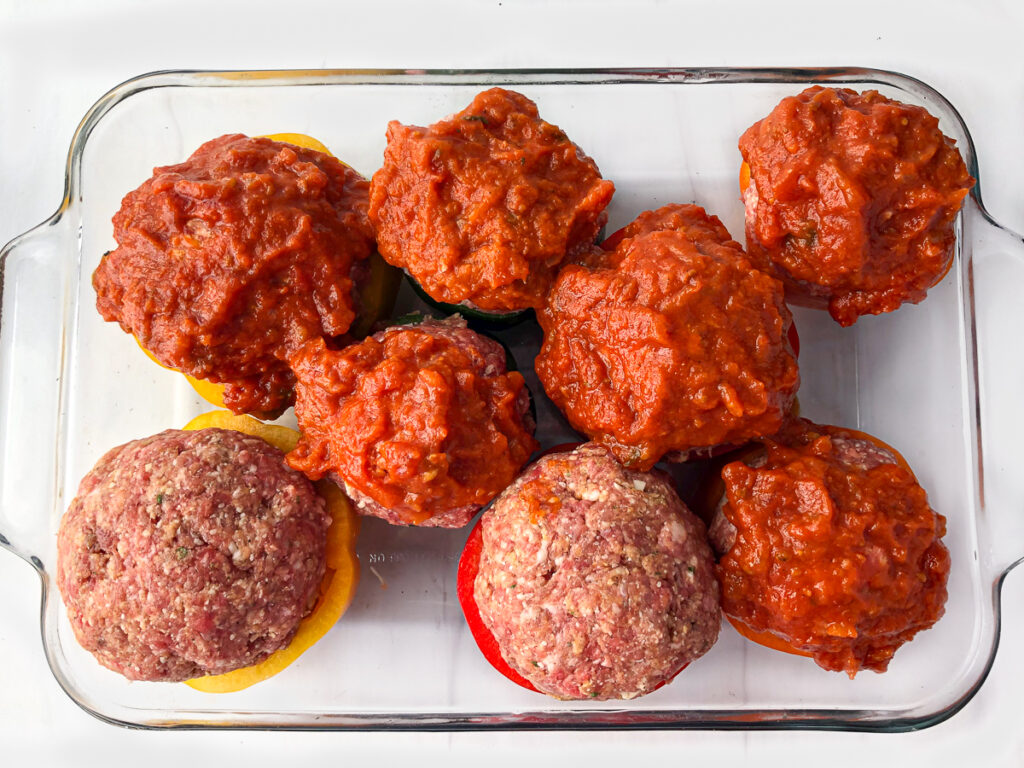 baking dish with peppers stuffed with big meatballs and some covered in sauce ready to bake
