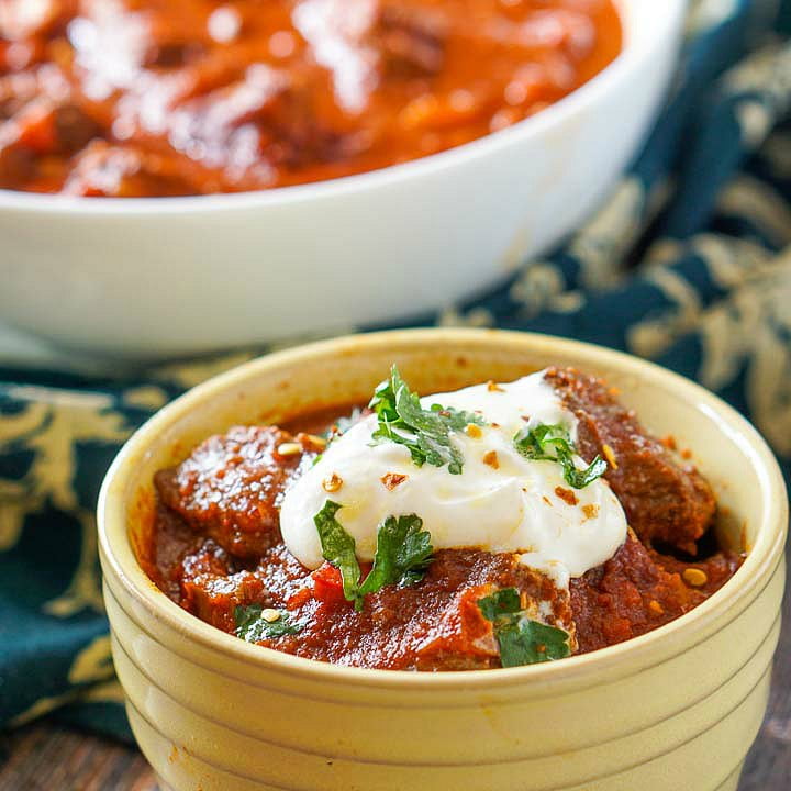 yellow bowl with chunky beef chili without beans topped with sour cream and cilantro 