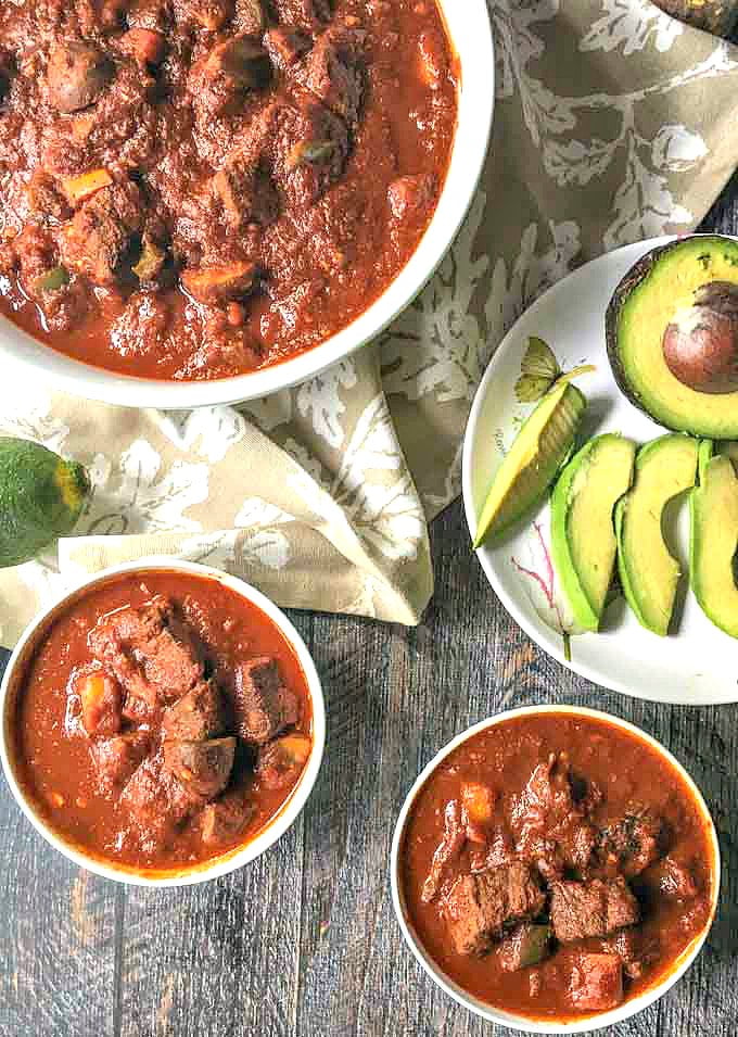 two small and one large white bowls with bean less beef chili and a sliced avocado on a plate