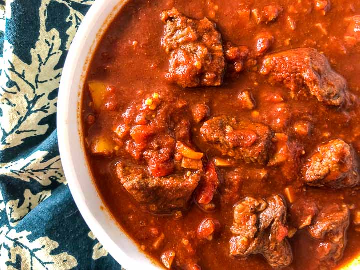 white bowl with chunky beef chili without beans on green leaf tea towel