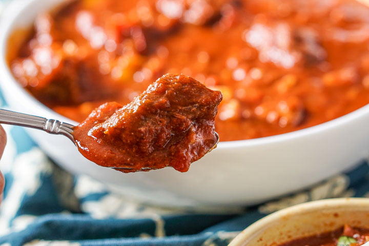 closeup of a spoon of the chunky beef chili with a white bowl in the background