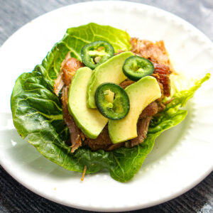 Closeup of a white plate with a lettuce wrap made with slow cooker pork carnitas.