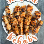 Aerial view of a white plate with marinated and grilled seafood kebabs and text.