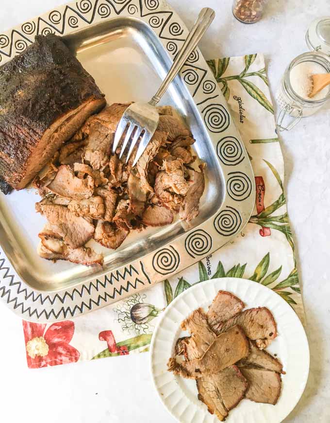 sliced smoked barbecue brisket on white plate with roast on a platter