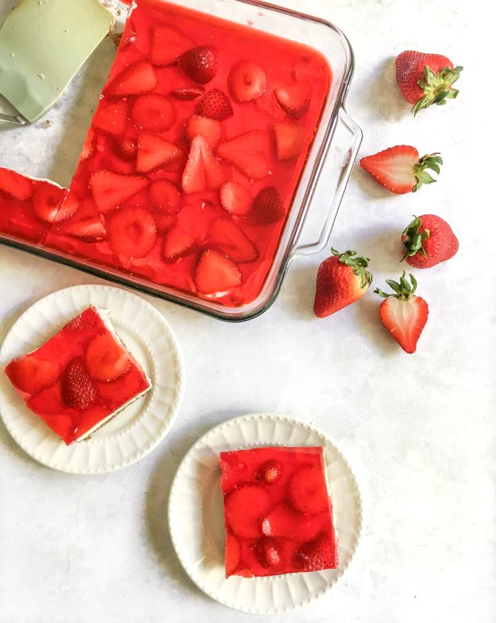 aerial view of a pan of keto strawberry jello pretzel salad with two white plates with slices and fresh strawberries