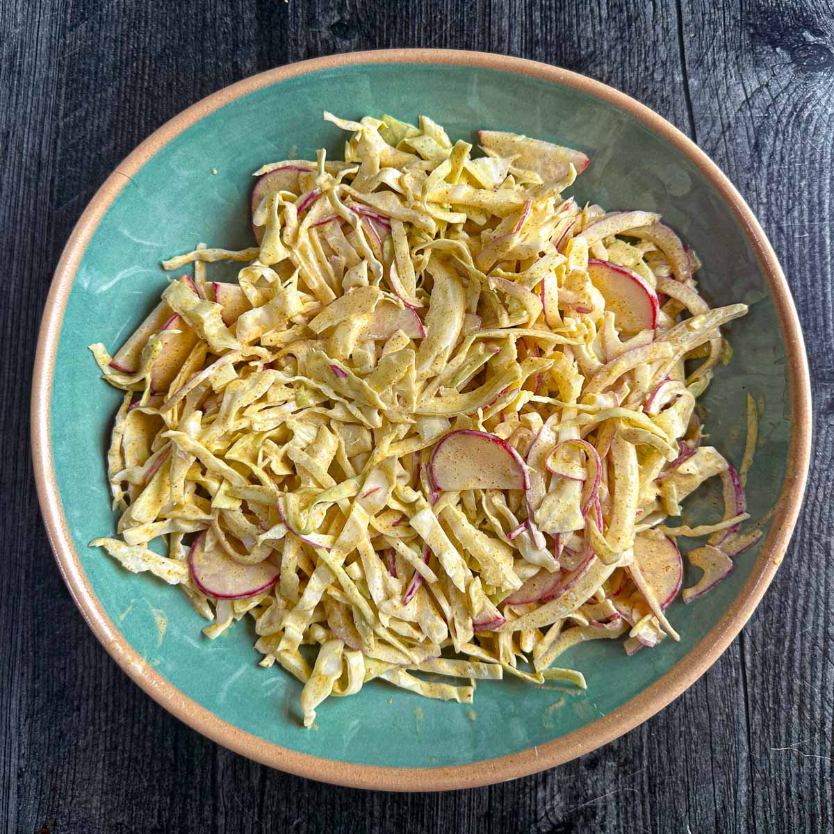 Aerial view of a aqua bowl with the radish and cabbage curried coleslaw.
