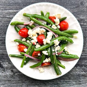 aerial view of a white plate with a serving of Greek green bean salad with feta cheese