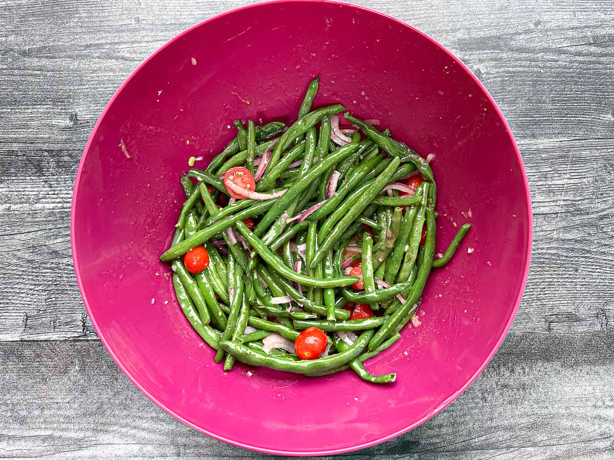 pink bowl with mixed green beans and tomatoes in dressing